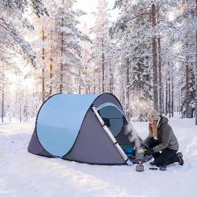En hiver, dans le bois, une femme cuit repas devant sa tente camping popup express