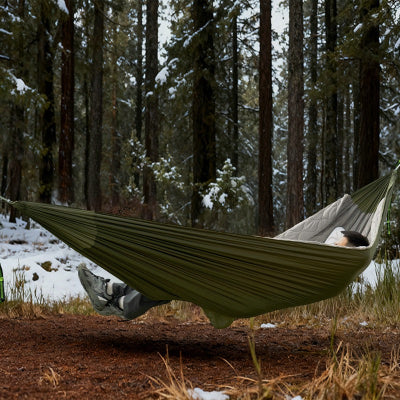 Forêt de conifères, un homme dans son hamacsac de couchage isolant 3 couches