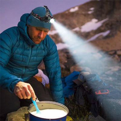 Homme prépare son repas en montagne avec sa lampe frontale puissante