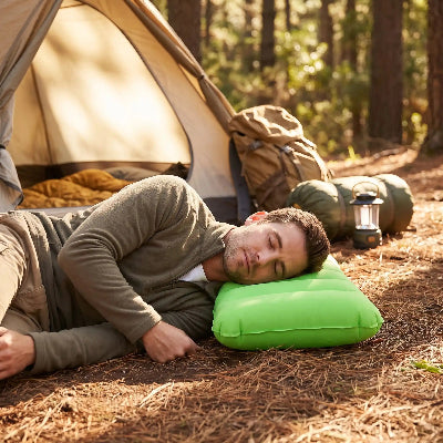 Un homme en camping sur le sol devant sa tente endormi sur un oreiller gonflable camping ultra-compact vert