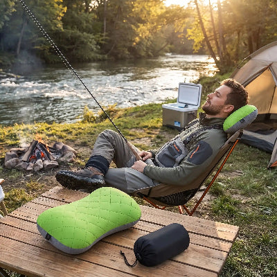 Un pêcheur se repose sur une chaise, à côté du ruisseau, avec oreiller gonflable ergonomique compact vert sur une table.