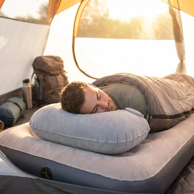 Homme couché dans sa tente, face contre terre, la tête sur son oreiller gonflable ergonomique gris.