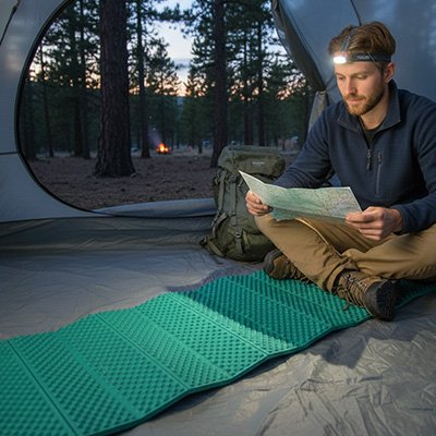 Assis sur son tapis de sol camping ultra réistant, dans tente, il se prépare pour la randonnée de demain.